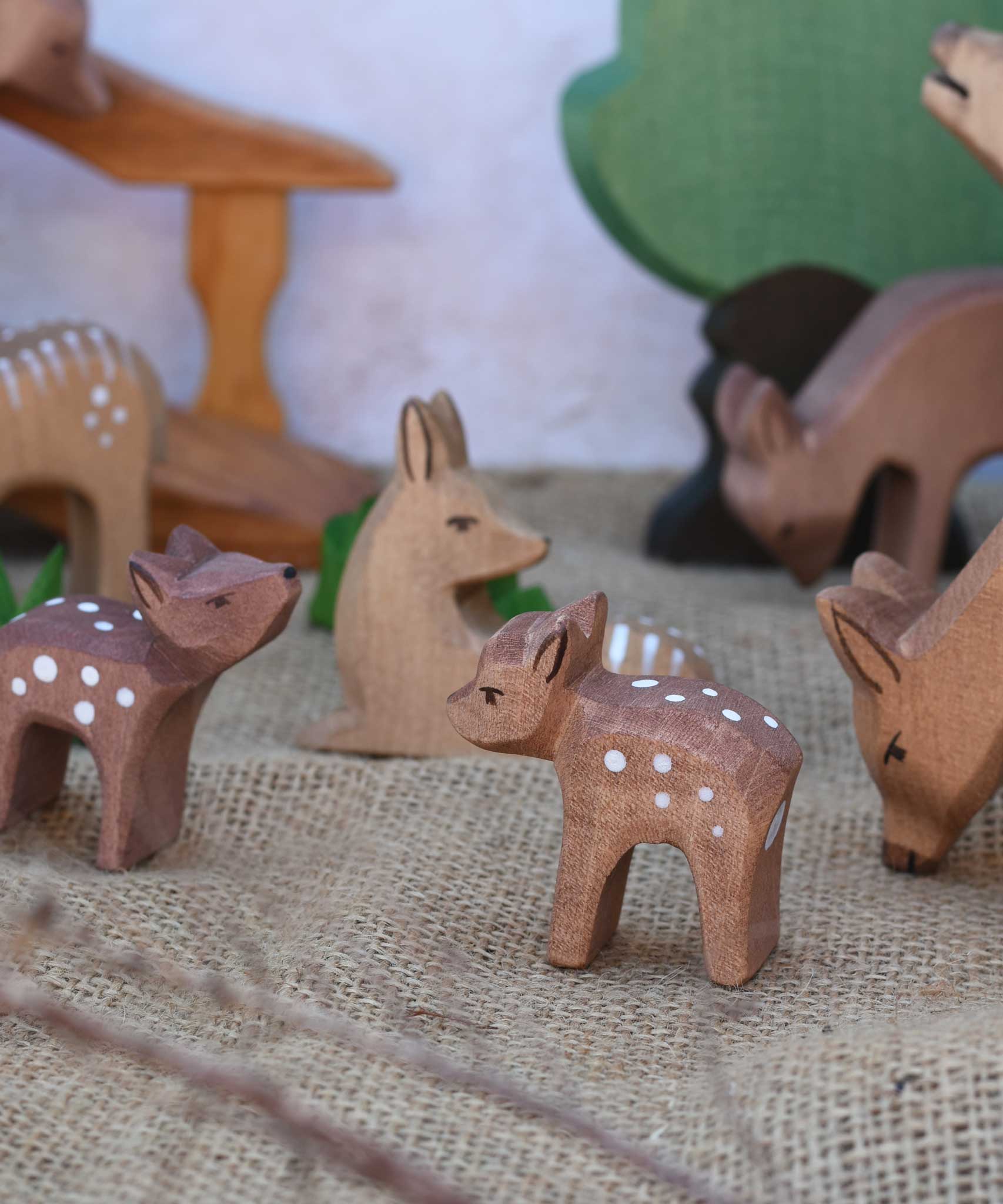 An Ostheimer Small Deer With Head Low placed in a small world play scene with lots of other deer and fawn figures. Ostheimer wooden toy figures and scenery are available at Babipur. 
