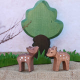 Two Ostheimer small deer figures placed in a small world play scene in front of green grass and oak tree figures. One deer has it's head facing up and the other's head is pointing down.