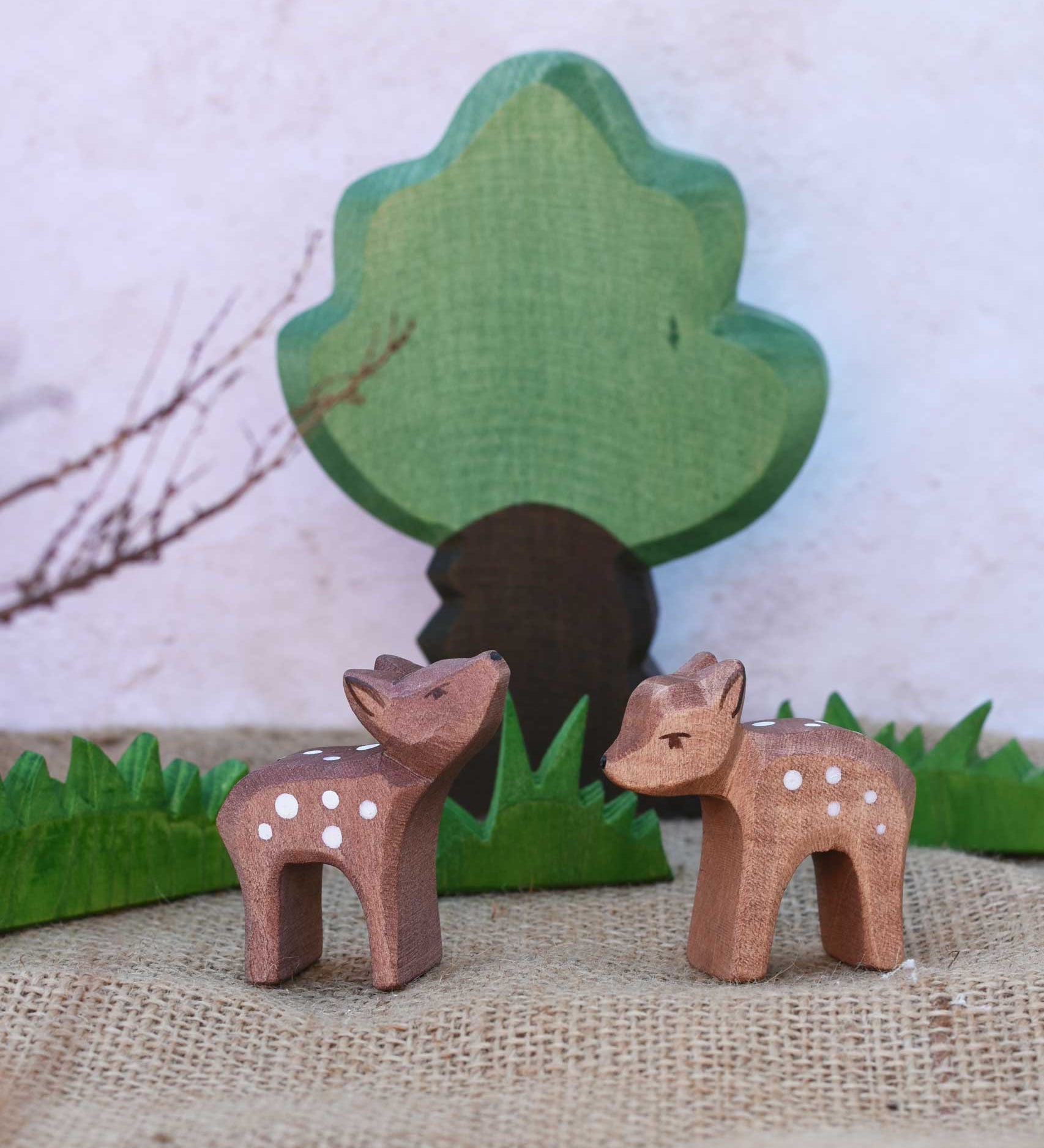 Two Ostheimer small deer figures placed in a small world play scene in front of green grass and oak tree figures. One deer has it's head facing up and the other's head is pointing down.
