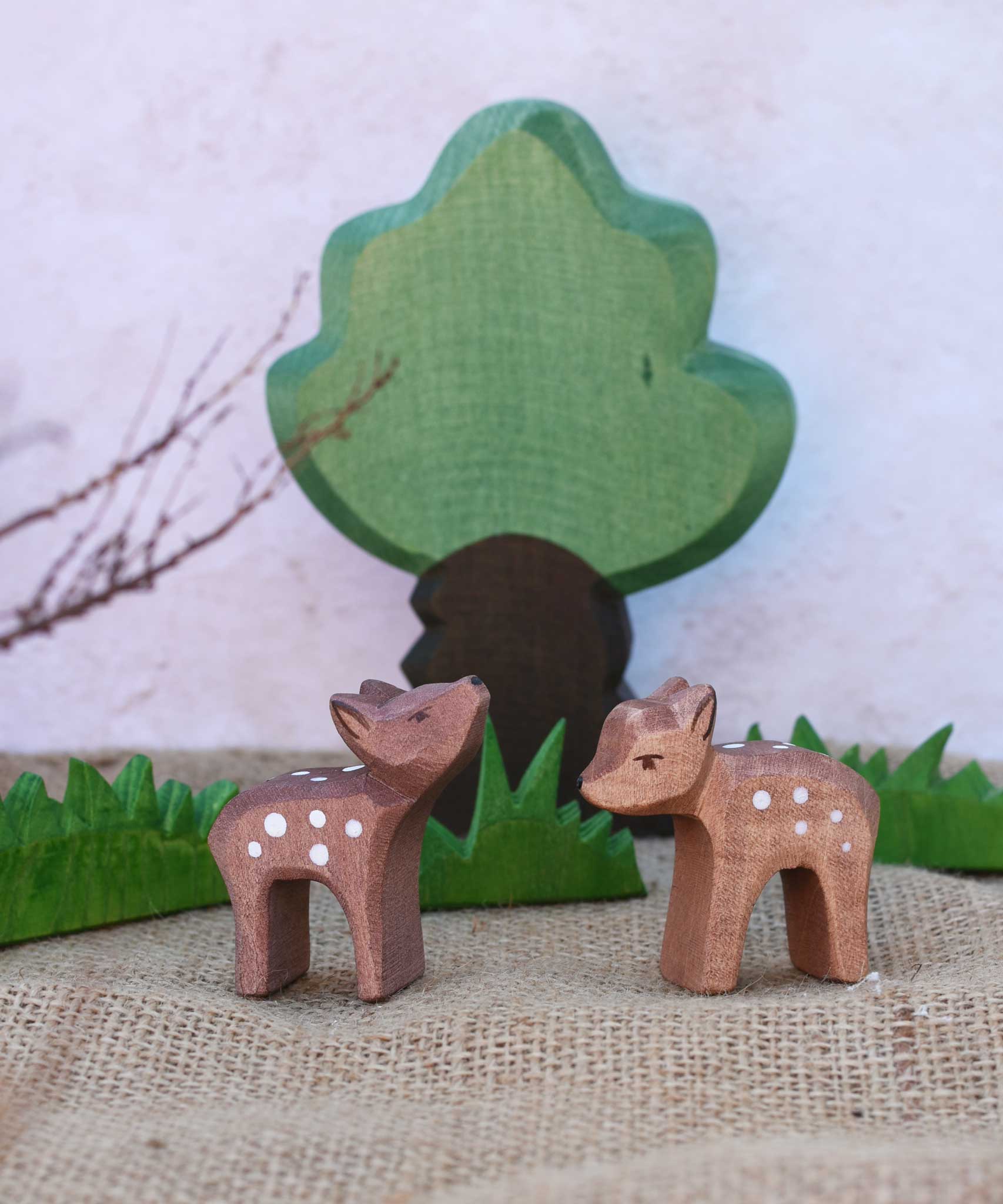 Two Ostheimer small deer figures placed in a small world play scene in front of green grass and oak tree figures. One deer has it's head facing up and the other's head is pointing down.
