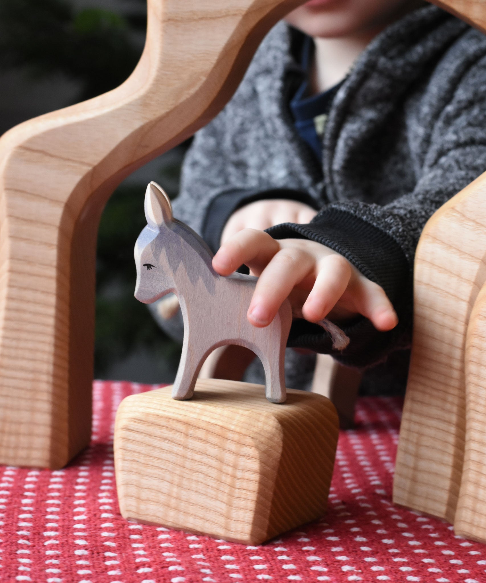 A child's hand reaching for the small Ostheimer donkey wooden toy figure.  Ostheimer's range of hand crafted, heirloom quality wooden toys are available to buy at Babipur. 