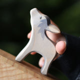 An Ostheimer small donkey wooden toy figure with it's head up being held in a child's hand and placed on a wooden surface. Ostheimer's range of hand crafted, heirloom quality wooden toys are available to buy at Babipur. 