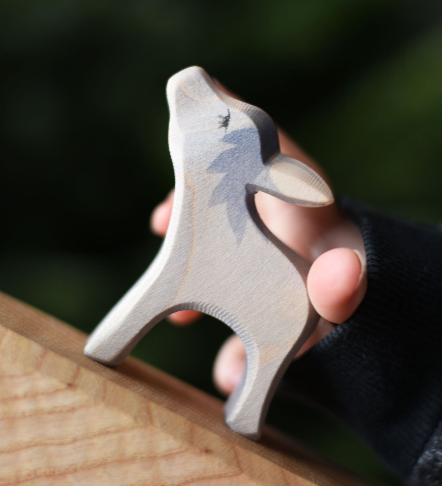 An Ostheimer small donkey wooden toy figure with it's head up being held in a child's hand and placed on a wooden surface. Ostheimer's range of hand crafted, heirloom quality wooden toys are available to buy at Babipur. 