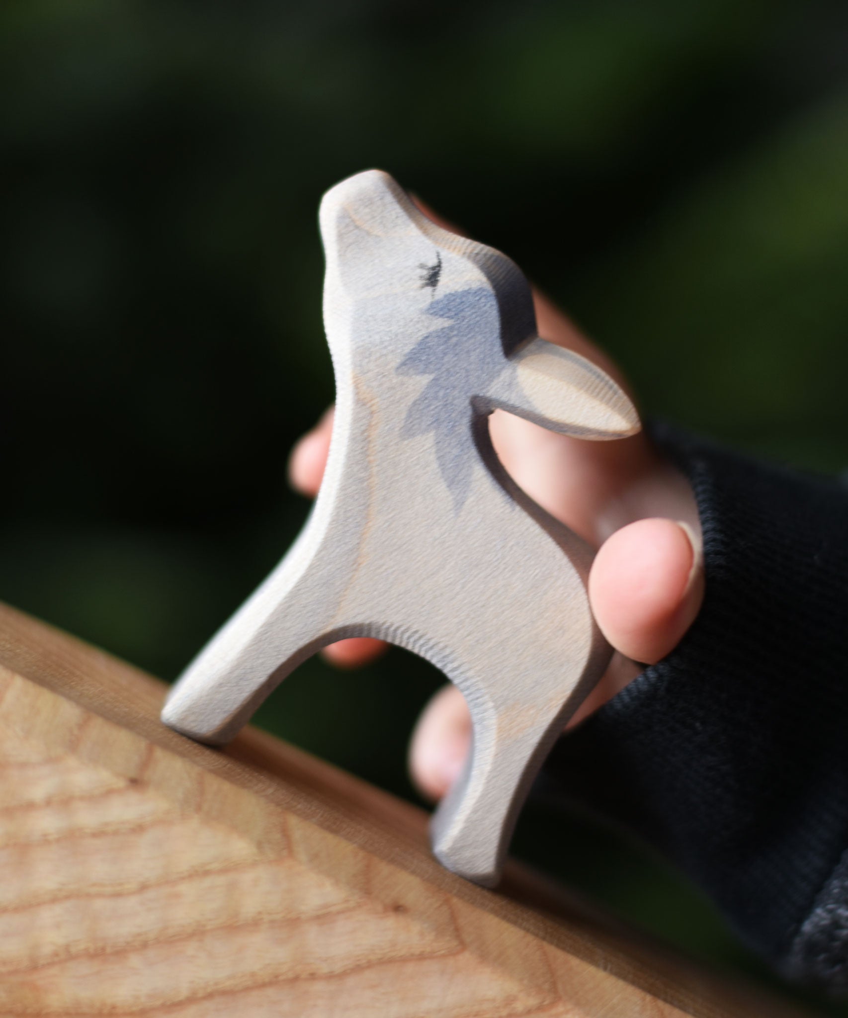 An Ostheimer small donkey wooden toy figure with it's head up being held in a child's hand and placed on a wooden surface. Ostheimer's range of hand crafted, heirloom quality wooden toys are available to buy at Babipur. 