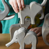 A child holding the Ostheimer small eating elephant wooden toy figure going to place it on top of the small elephant with trunk out. 
