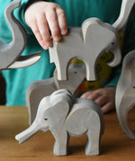 A child holding the Ostheimer small eating elephant wooden toy figure going to place it on top of the small elephant with trunk out. 