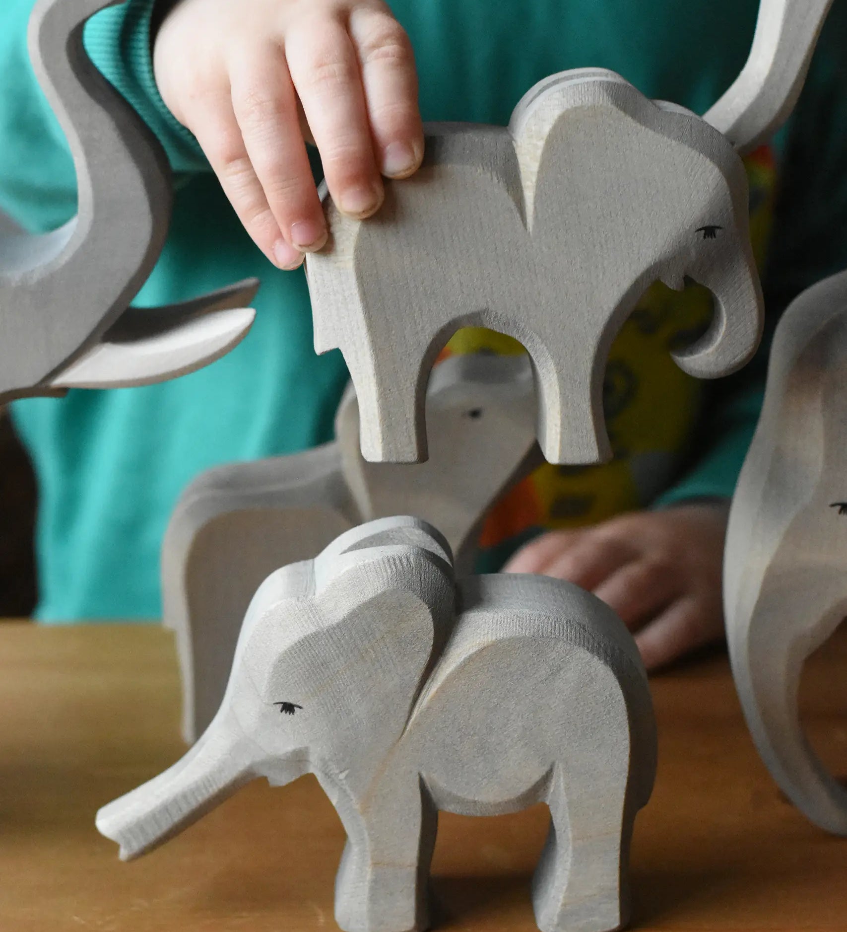 A child holding the Ostheimer small eating elephant wooden toy figure going to place it on top of the small elephant with trunk out. 
