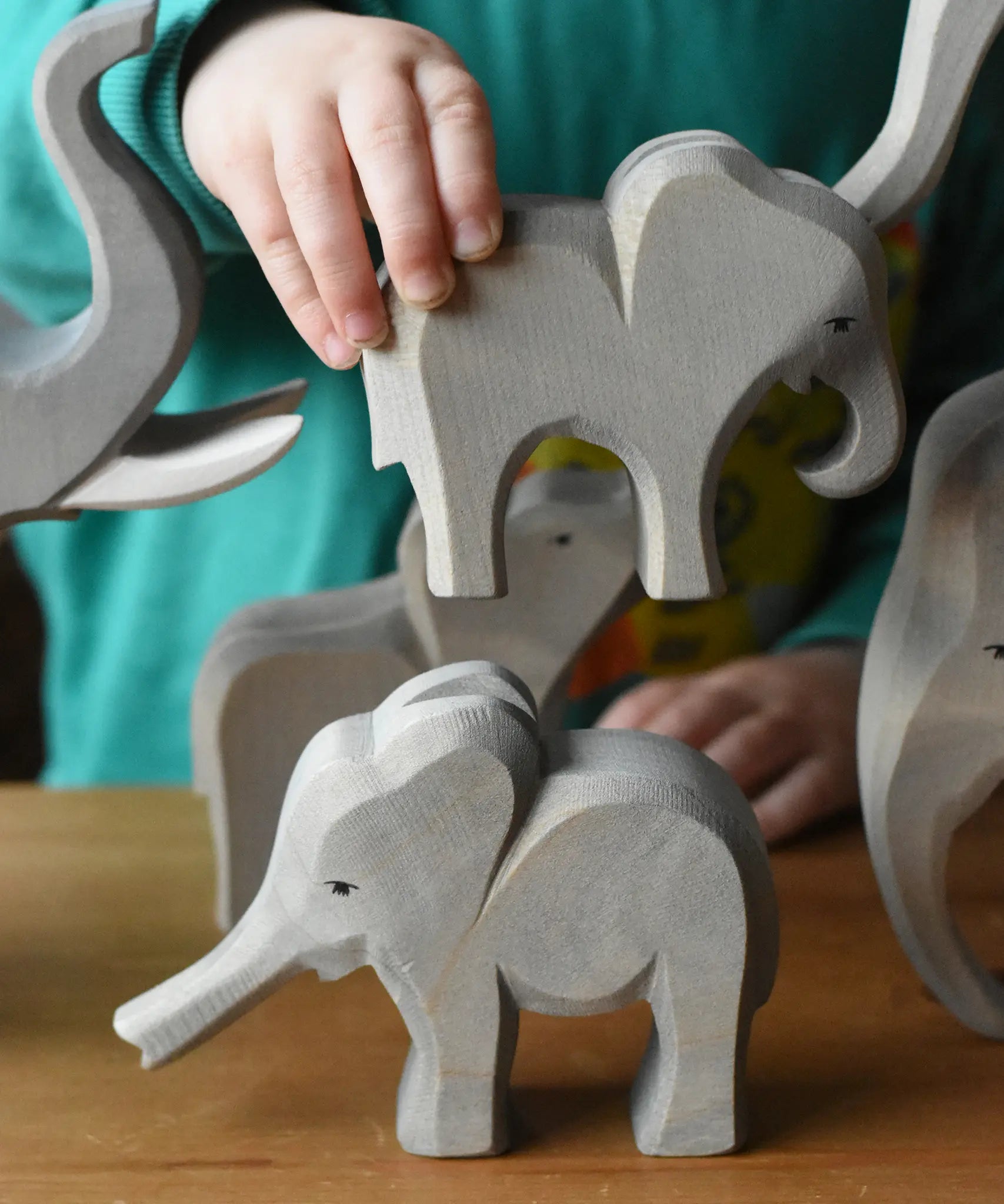 A child holding the Ostheimer small eating elephant wooden toy figure going to place it on top of the small elephant with trunk out. 