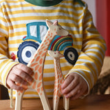 Child holding Ostheimer giraffe wooden toy figures. A running giraffe and small giraffe with head high. 