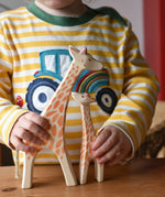 Child holding Ostheimer giraffe wooden toy figures. A running giraffe and small giraffe with head high. 