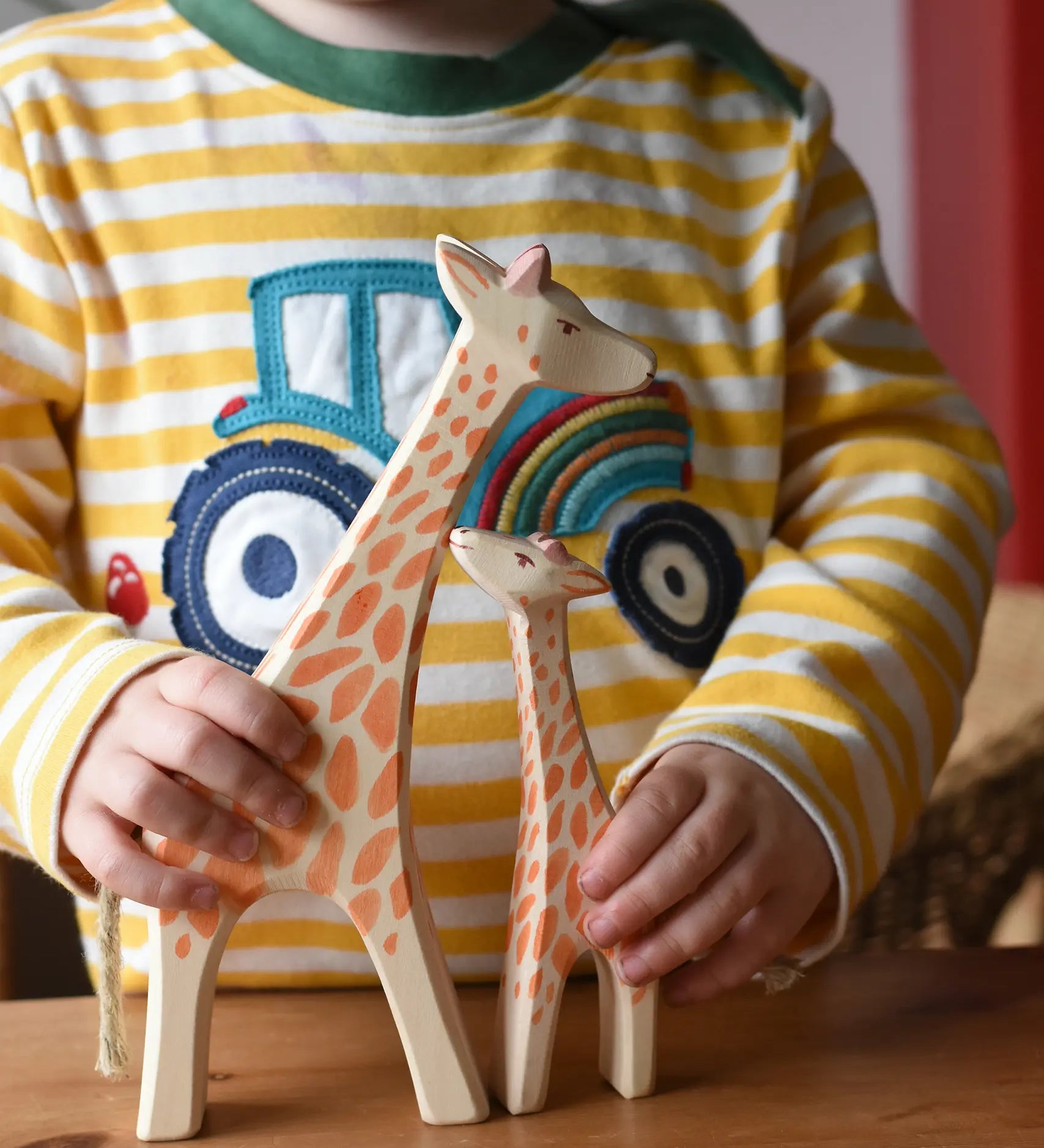 Child holding Ostheimer giraffe wooden toy figures. A running giraffe and small giraffe with head high. 