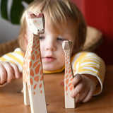 Ostheimer giraffe figures placed on a wooden surface in front of a child.