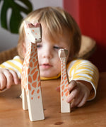 Ostheimer giraffe figures placed on a wooden surface in front of a child.