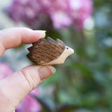 A small hedgehog wooden toy figure shown in an adult's hand to show scale. Check out our full range of expertly crafted wooden toy figures and scenery here at Babipur.