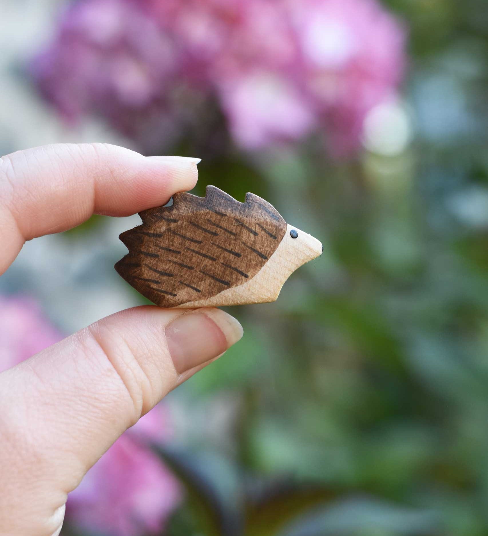 A small hedgehog wooden toy figure shown in an adult's hand to show scale. Check out our full range of expertly crafted wooden toy figures and scenery here at Babipur.
