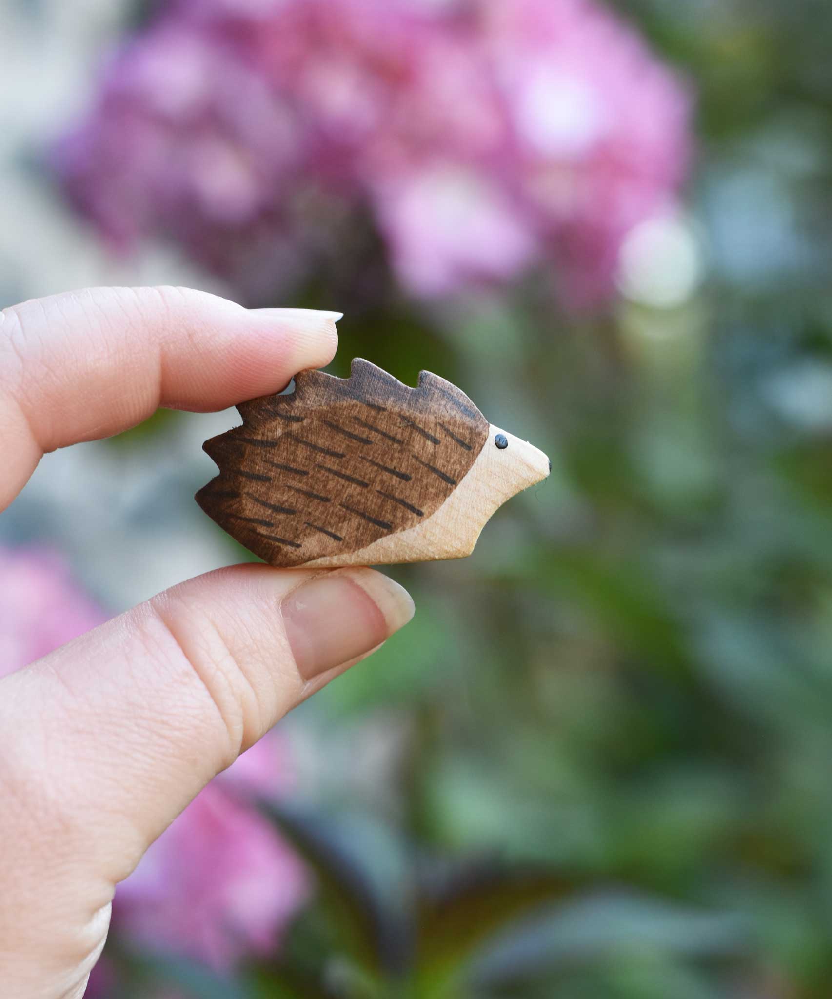 A small hedgehog wooden toy figure shown in an adult's hand to show scale. Check out our full range of expertly crafted wooden toy figures and scenery here at Babipur.