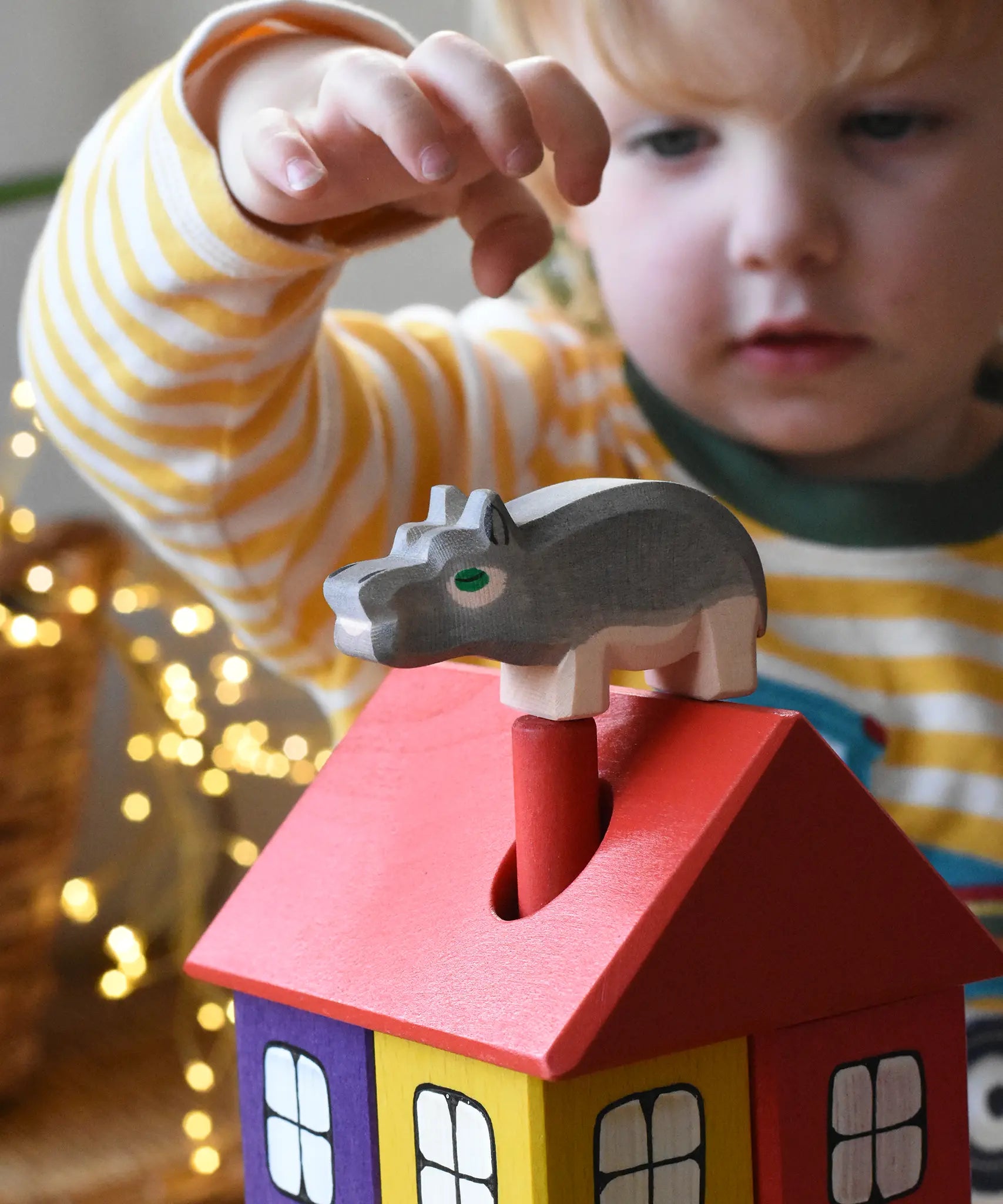 Ostheimer small hippopotamus wooden toy figure placed on the roof of the coloured house by a child. 
