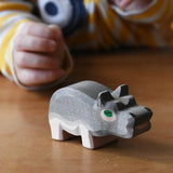 Ostheimer small hippopotamus wooden toy figure placed on a wooden surface. Child reaching for it in the background. 