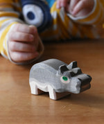 Ostheimer small hippopotamus wooden toy figure placed on a wooden surface. Child reaching for it in the background. 