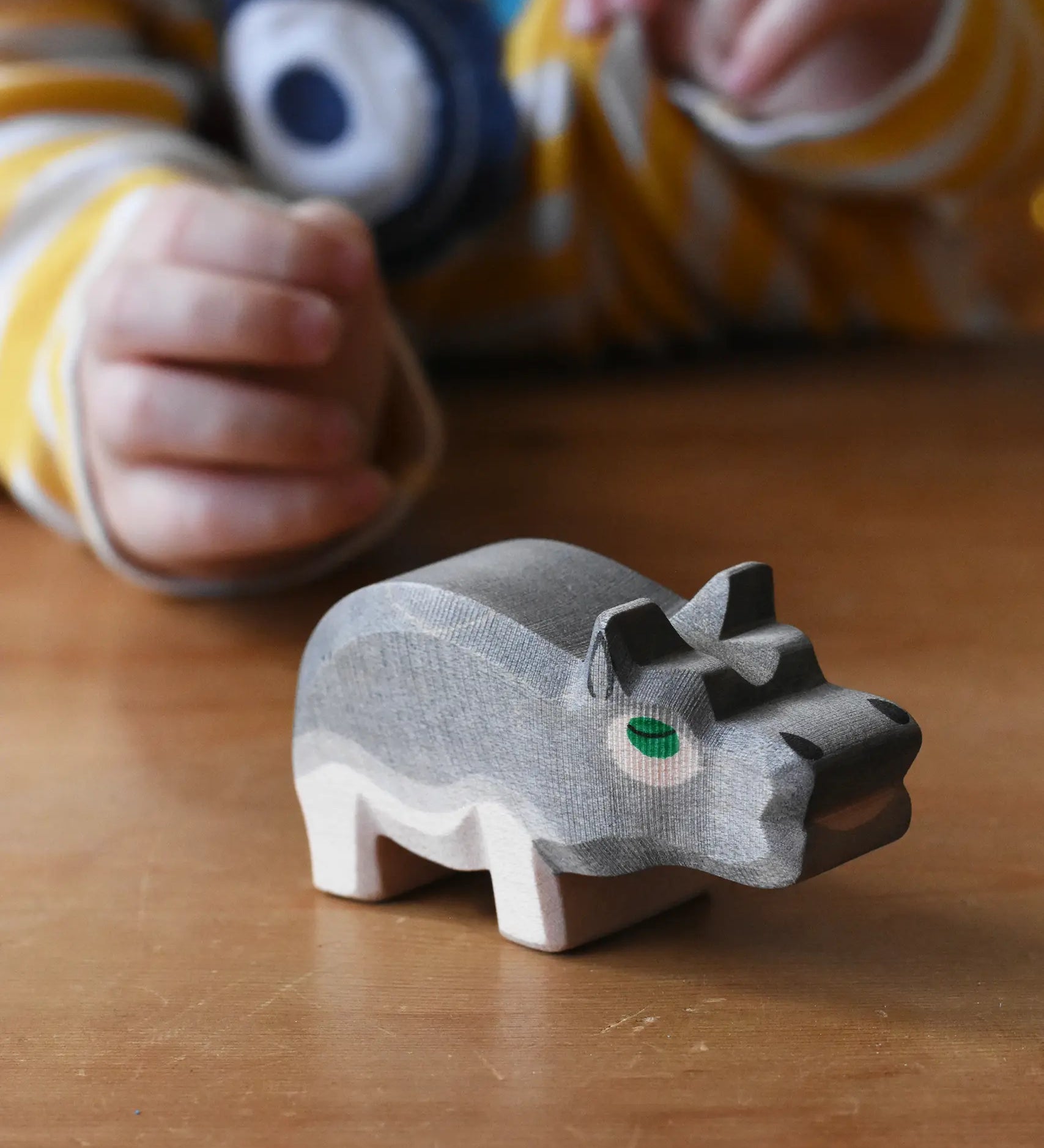 Ostheimer small hippopotamus wooden toy figure placed on a wooden surface. Child reaching for it in the background. 