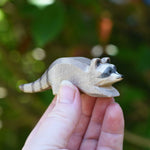 A small Ostheimer raccoon shown in an adult's hand for scale. Check out our full range of expertly crafted wooden toy figures and scenery here at Babipur.