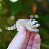 A small Ostheimer raccoon shown in an adult's hand for scale. Check out our full range of expertly crafted wooden toy figures and scenery here at Babipur.