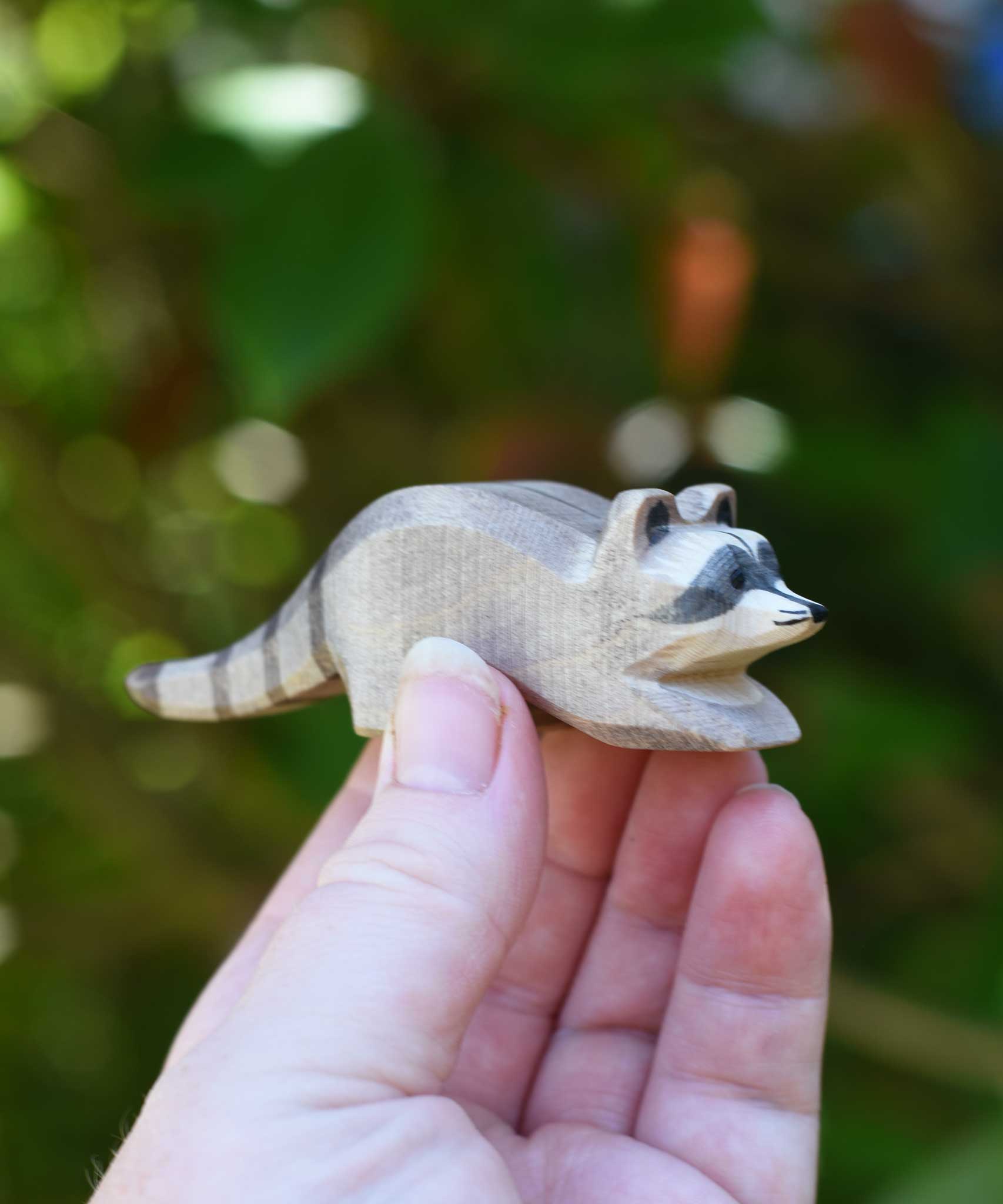 A small Ostheimer raccoon shown in an adult's hand for scale. Check out our full range of expertly crafted wooden toy figures and scenery here at Babipur.