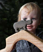 The small Ostheimer rhino wooden toy figure placed on a wooden cave shaped piece. A child can be seen looking on in the background. These wooden figures are part of a wide range of expertly hand crafted wooden toys here at Babipur.