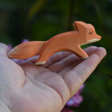 A small Ostheimer running red fox wooden toy figure shown in an adult's hand for scale. Check out our full range of expertly crafted wooden toy figures and scenery here at Babipur.