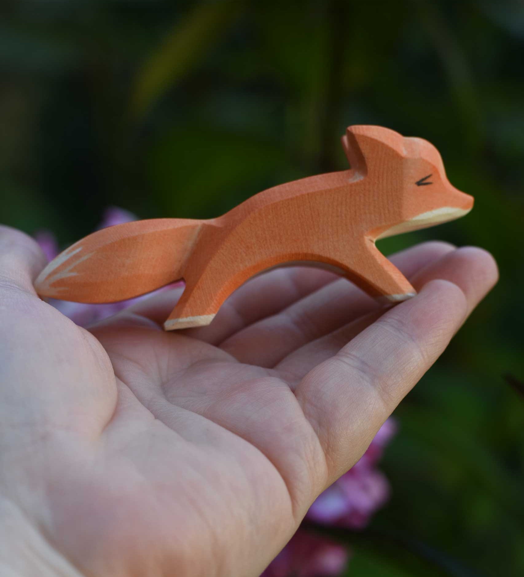 A small Ostheimer running red fox wooden toy figure shown in an adult's hand for scale. Check out our full range of expertly crafted wooden toy figures and scenery here at Babipur.