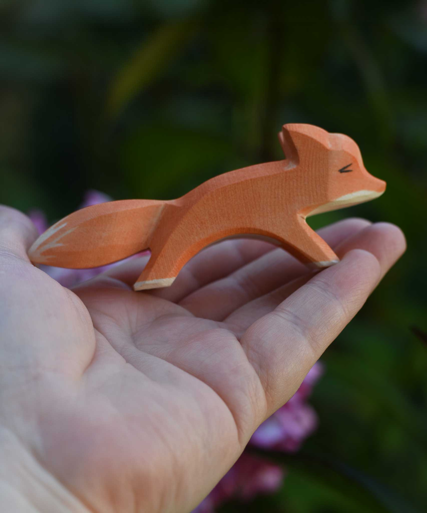 A small Ostheimer running red fox wooden toy figure shown in an adult's hand for scale. Check out our full range of expertly crafted wooden toy figures and scenery here at Babipur.