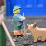 Ostheimer small shepherd boy wooden toy figure placed on a stone wall with a German shepherd blurred in the foreground. 
