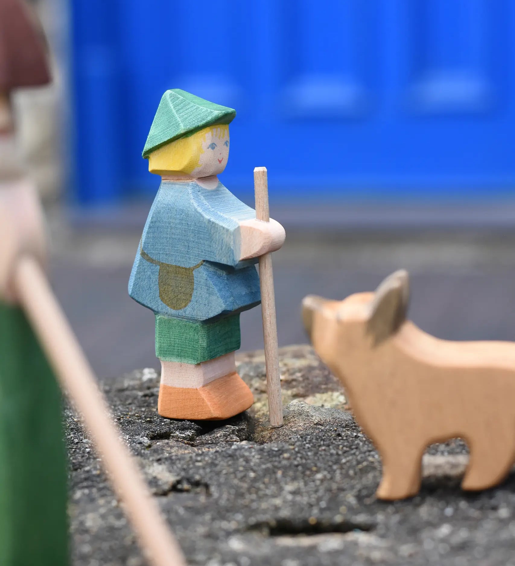 Ostheimer small shepherd boy wooden toy figure placed on a stone wall with a German shepherd blurred in the foreground. 