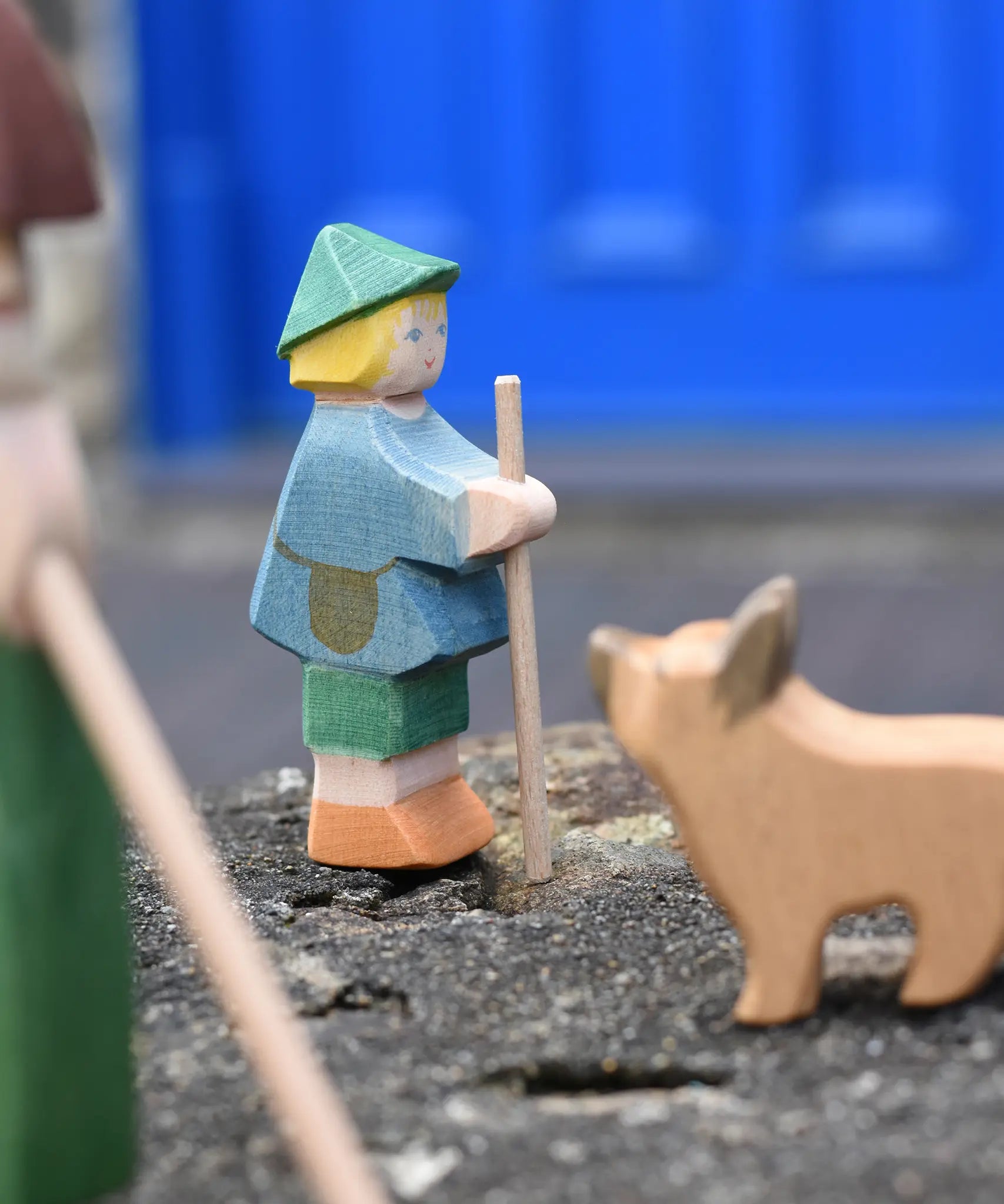 Ostheimer small shepherd boy wooden toy figure placed on a stone wall with a German shepherd blurred in the foreground. 