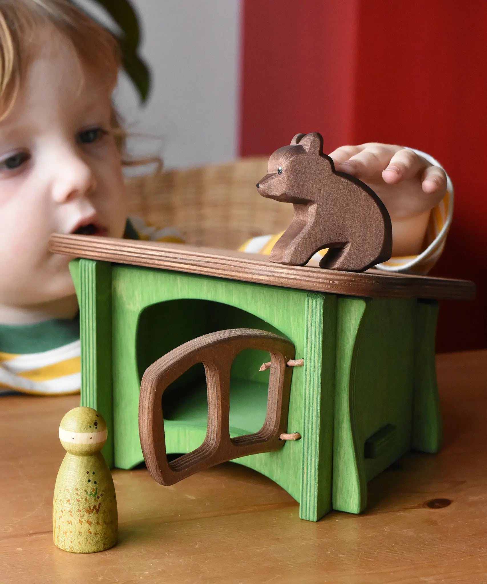 Ostheimer small sitting brown bear wooden toy figure placed on the roof of a green hutch toy with a Grapat animal Nin placed in front of the hutch. 