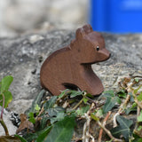 Ostheimer small sitting brown bear wooden toy figure placed on a stone wall outdoors. 