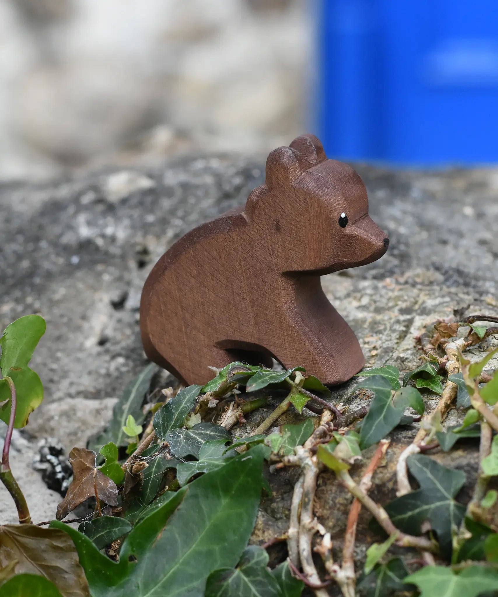 Ostheimer small sitting brown bear wooden toy figure placed on a stone wall outdoors. 