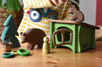 Ostheimer bear and small sitting brown bear wooden toy figures in a small world play scene with the green hutch, small spruce tree, Grapat rings and animal Nins and small Kraul basket.