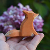 An Ostheimer small red sitting fox shown in an adult's hand for scale. Check out our full range of expertly crafted wooden toy figures and scenery here at Babipur.
