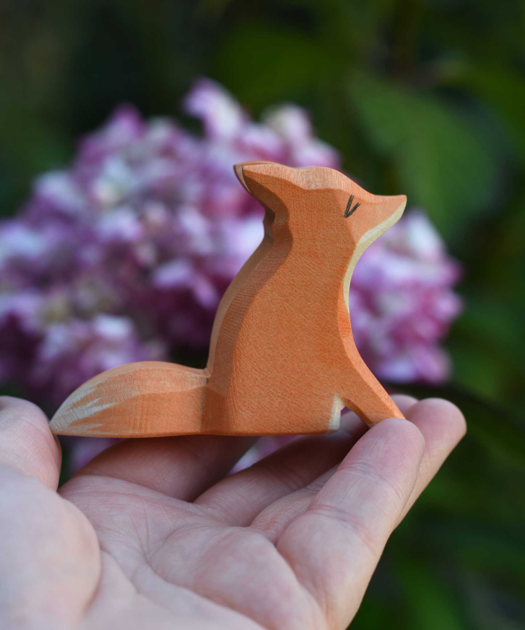 An Ostheimer small red sitting fox shown in an adult's hand for scale. Check out our full range of expertly crafted wooden toy figures and scenery here at Babipur.