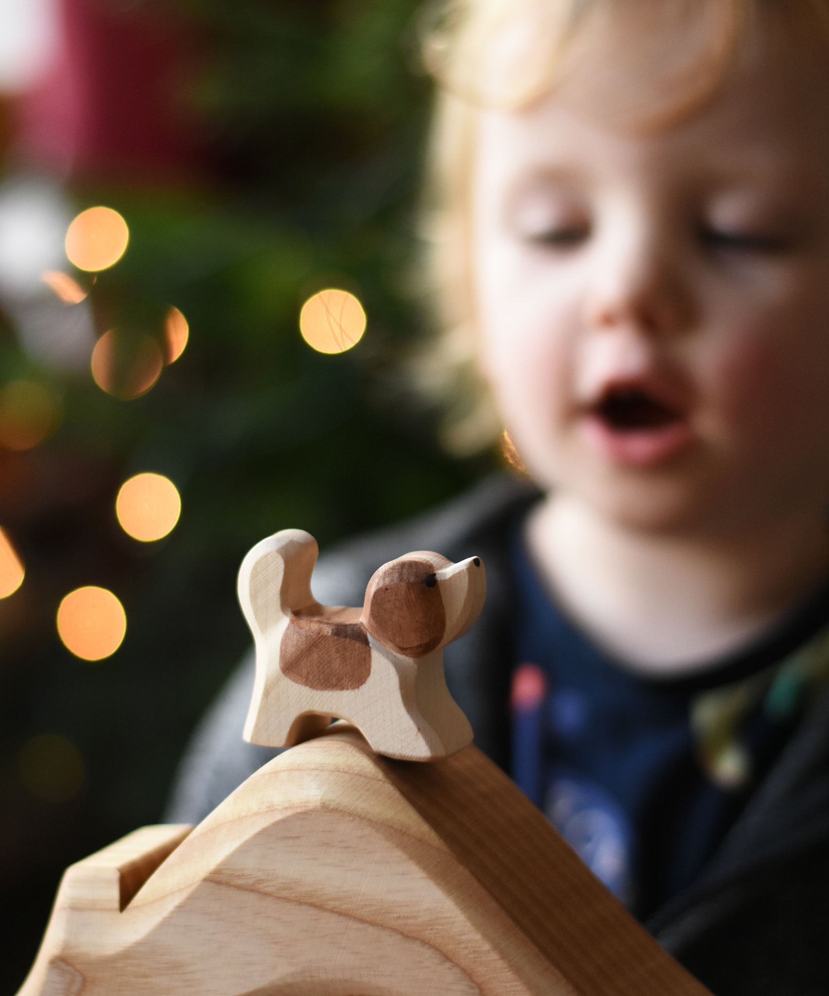An Ostheimer small St Bernard dog wooden toy figure placed on a wooden house shaped piece. A child can be seen in the background. These wooden figures are part of a wide range of expertly hand crafted wooden toys here at Babipur. 