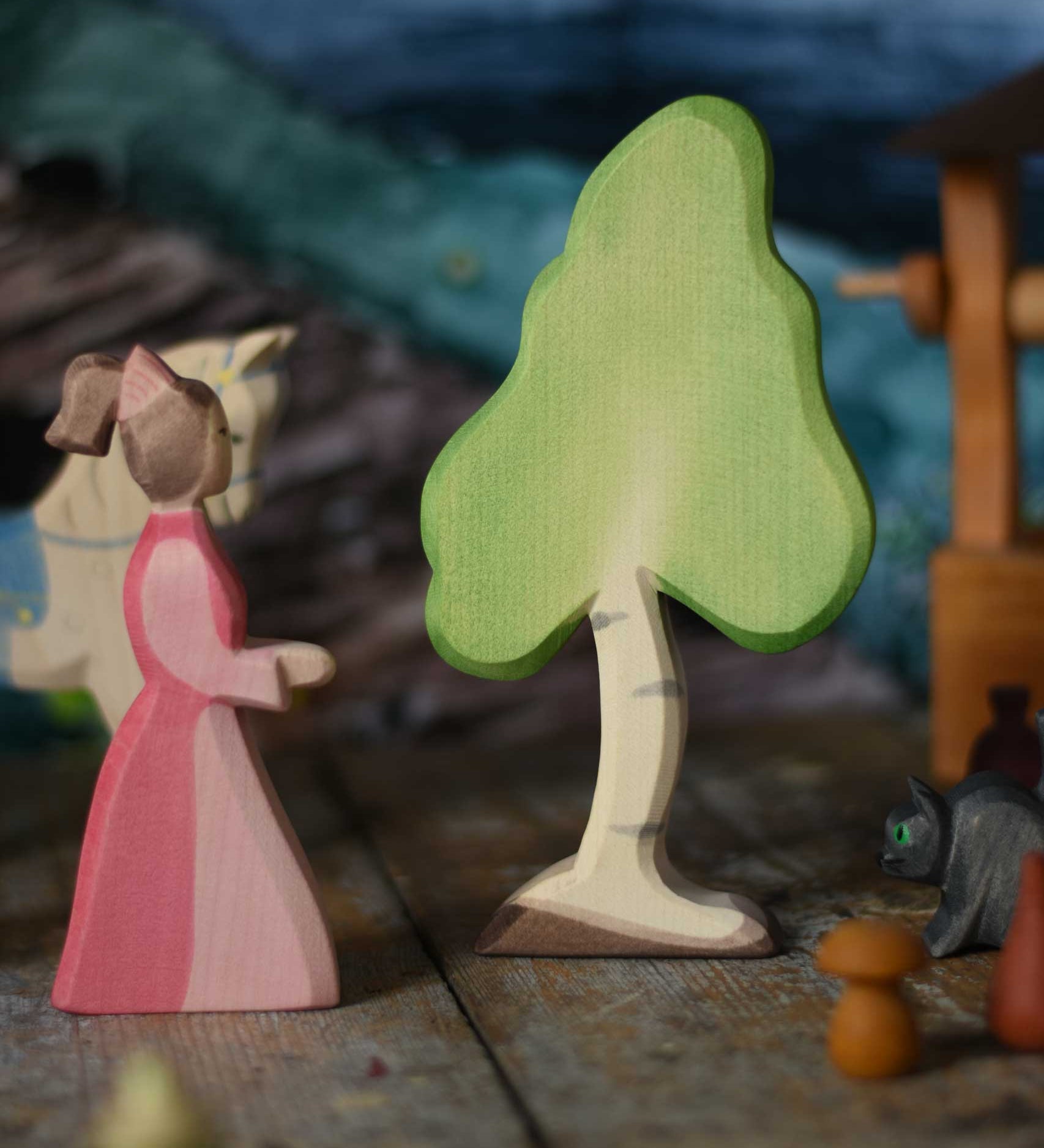 A small Ostheimer birch tree placed on a wooden surface in the middle of a small world play scene next to a lady-in-waiting-figure. These wooden figures are part of a wide range of expertly hand crafted wooden toys here at Babipur. 