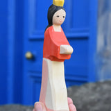 Ostheimer snow white wooden toy figure in an adult's hand held up in front of a blue door.