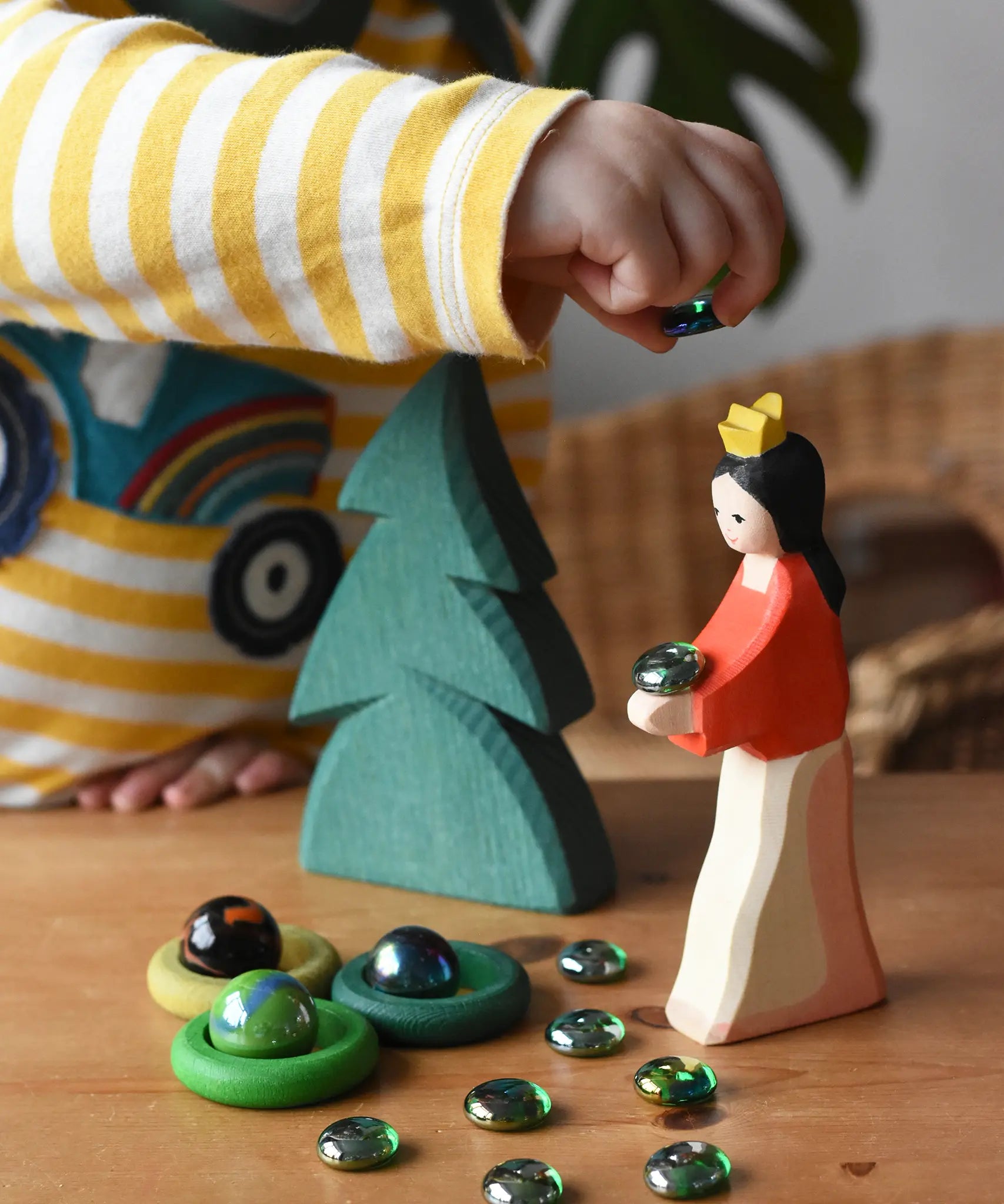 Ostheimer snow white wooden toy figure placed in a small world play scene with a small spruce tree, Billes flat marbles and green Grapat rings.