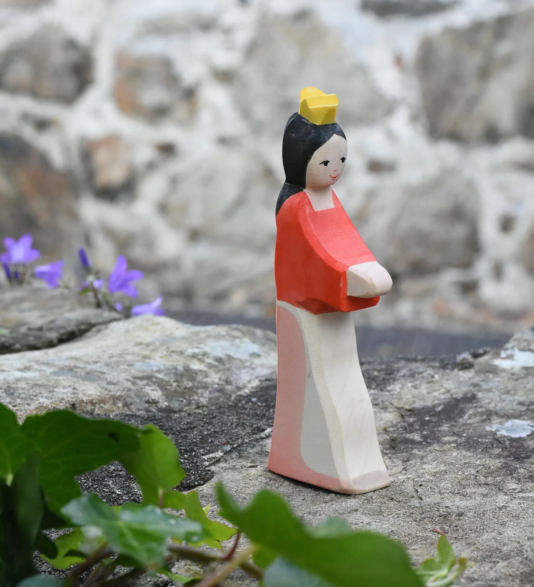 Ostheimer Snow White wooden toy figure placed on a stone wall outdoors. 