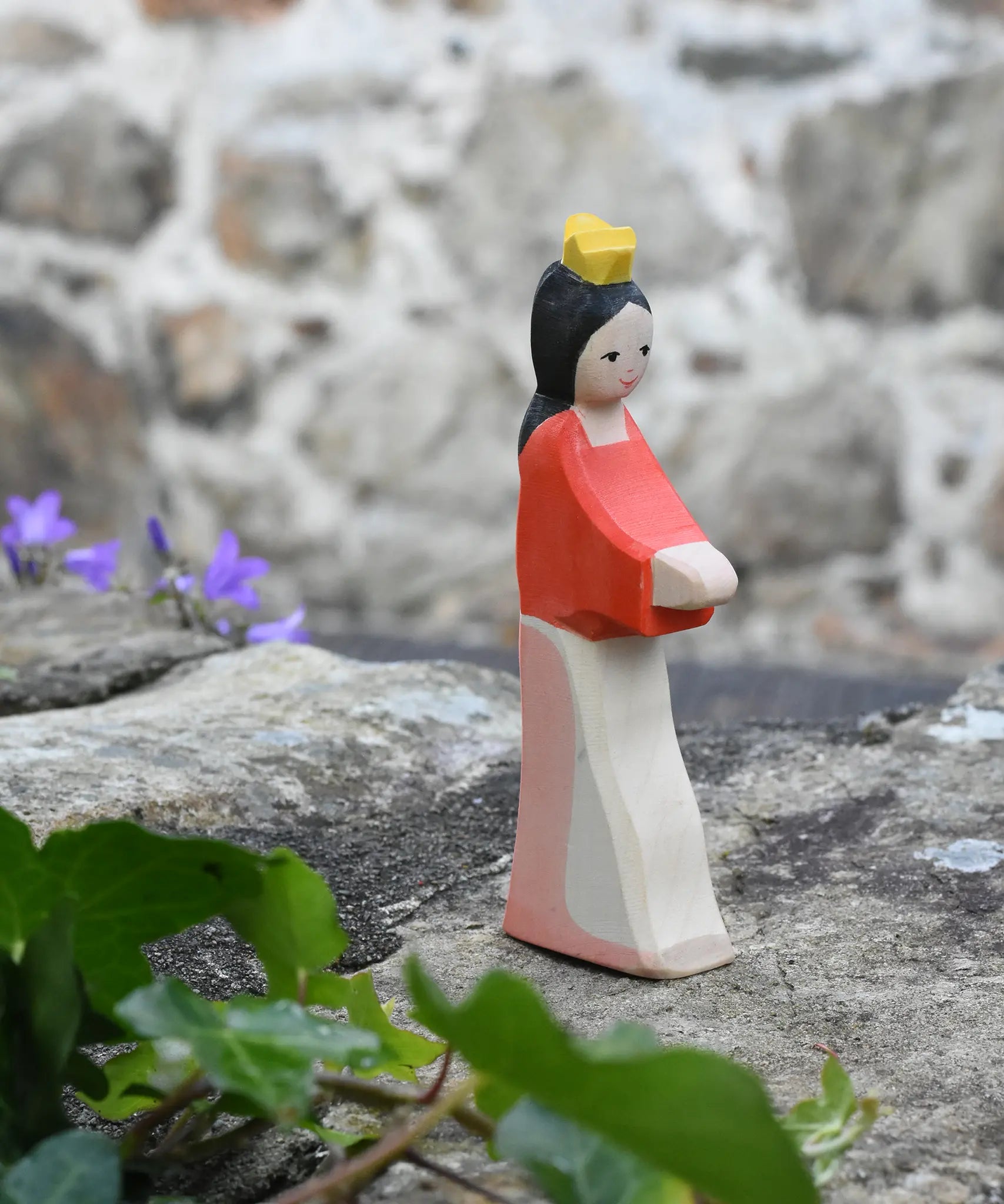 Ostheimer Snow White wooden toy figure placed on a stone wall outdoors. 