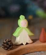 An Ostheimer hand made and hand painted wooden snowdrop Flower Child figure toy placed on a natural Grimm's celebration ring. These flower child wooden figures are part of a wide range of expertly hand crafted wooden toys here at Babipur. 