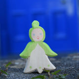 An Ostheimer hand made and hand painted wooden snowdrop Flower Child figure toy placed on a stone wall outdoors. These flower child wooden figures are part of a wide range of expertly hand crafted wooden toys here at Babipur. 
