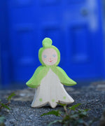 An Ostheimer hand made and hand painted wooden snowdrop Flower Child figure toy placed on a stone wall outdoors. These flower child wooden figures are part of a wide range of expertly hand crafted wooden toys here at Babipur. 
