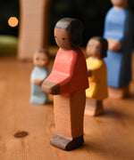 An Ostheimer son wooden toy figure with brown skin placed at the front of a small world play scene. These wooden figures are part of a wide range of expertly hand crafted wooden toys here at Babipur.